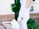 a white lace sheath wedding dress with an open back and long sleeves is a stylish idea
