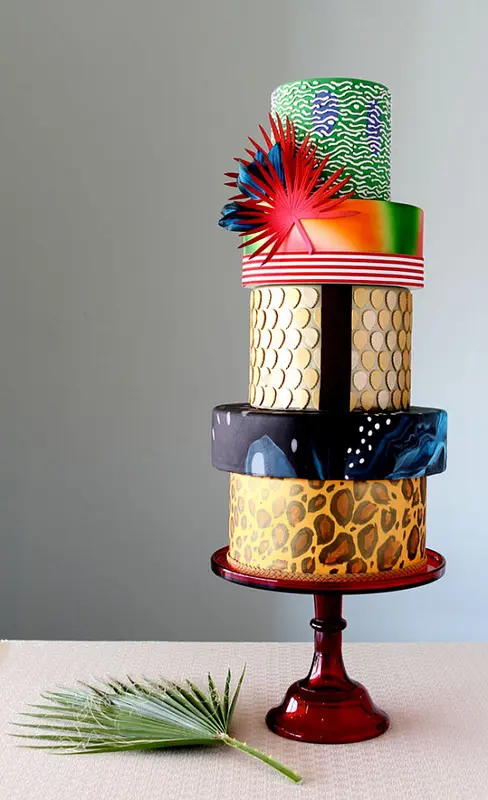 a colorful and bright multi-tier wedding cake with various colors and prints, with patterns and faux leaves on top is a lovely idea for a bold and quirky wedding