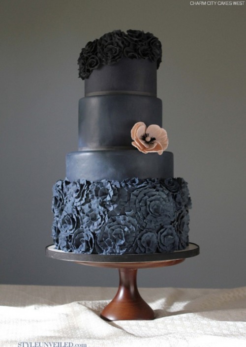 a black wedding cake with sleek tiers, sugar blooms on top and on the lowest tier, with a pink sugar bloom for a color accent