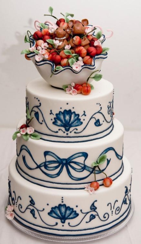 a white wedding cake with painted ribbons and bows, with sugar blooms and leaves, some cherries, a bowl with cherries on top and a chocolate mouse in the bowl is a lovely idea