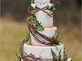 a woodland wedding cake with sugar leaves, berries and twigs completely wrapping up the cake, arrows and a love bird cake topper