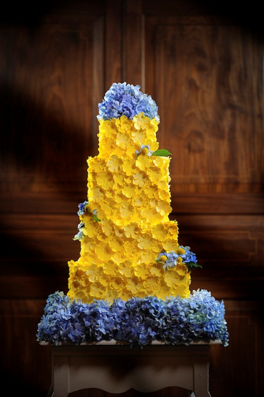 A yellow floral wedding cake decorated with fresh blue blooms is a catchy idea for a spring or summer wedding done in a bold color palette