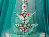 a whimsical turquoise wedding cake with three tiers and three balls on top, with a heart and some lace detailing plus some ruffles and bold spots