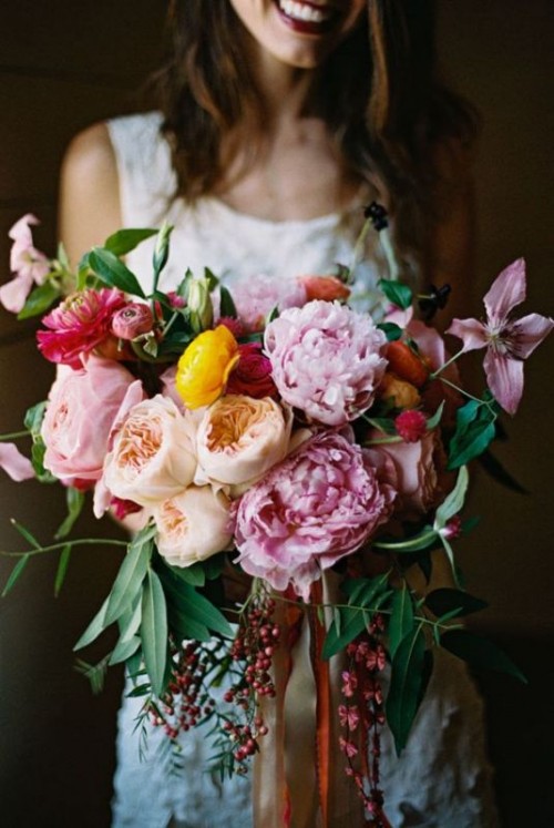 a beautiful and bold wedding bouquet of pink, coral and peachy peonies, greenery and berries plus ranunculus is a bold idea for a summer wedding