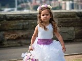 a flower girl wearing a sleeveless white maxi dress with a radiant orchid sash and a matching floral crown plus a basket with blooms