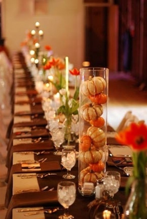 colorful bloom centerpieces and tall clear vases with pumpkins plus candles make the tables look even longer