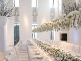 white bloom centerpieces and an overhead decoration visually elongate the tables evne more