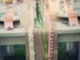 a burlap runner with colorful ribbons, pompoms and lace is a bold decoration for a boho wedding table