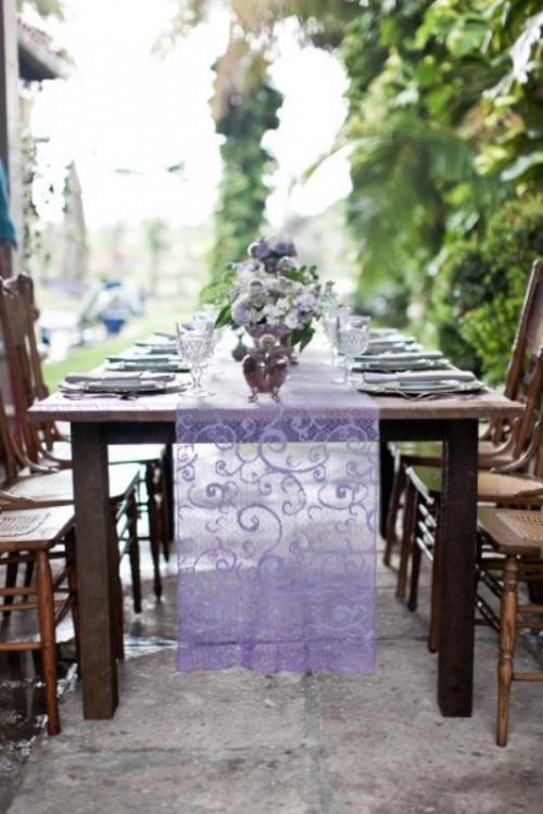 a purple lace wedding table runner highlights the purple floral centerpieces in vintage silver teapots