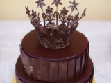 a round chocolate wedding cake with additional chocolate shards covering it and a fantastic chocolate crown is a refined and royal-inspired idea of a dessert