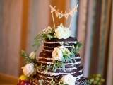 a naked chocolate wedding cake with white blooms, greenery, a banner topper and fresh fall fruit around is a gorgeous fall wedding dessert
