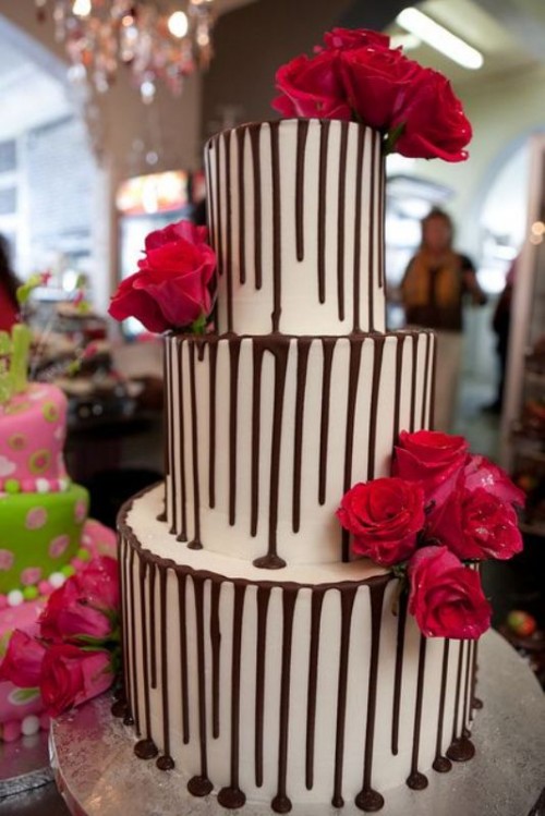 a bold-looking buttercream wedding cake with chocolate drip and red blooms is a cool and bold idea for a modern wedding with a touch of color