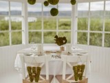 a neutral reception space done in white, with moss balls hanging over the table, neutral table decor and chairs decorated with burlap ties and moss monograms