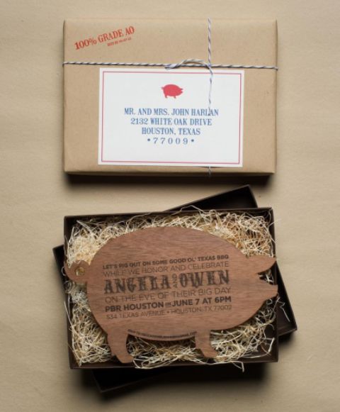 a creative rehearsal dinner invitation of a box covered in kraft paper, with straw and a wooden pig invitation for a BBQ rehearsal