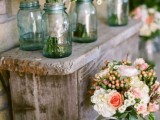a wooden bench with lush floral centerpieces in pink and white and in blue jars
