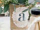 a rustic rehearsal dinner centerpiece of a tin can wrapped with burlap, a doily and baby’s breath