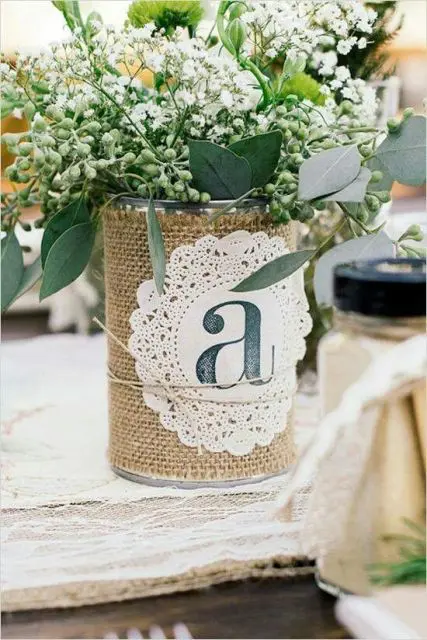 a rustic rehearsal dinner centerpiece of a tin can wrapped with burlap, a doily and baby's breath