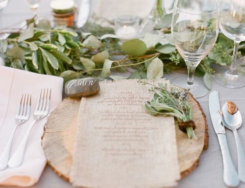 a cozy and chic rustic setting with a wood slice, a greenery runner and some pebbles