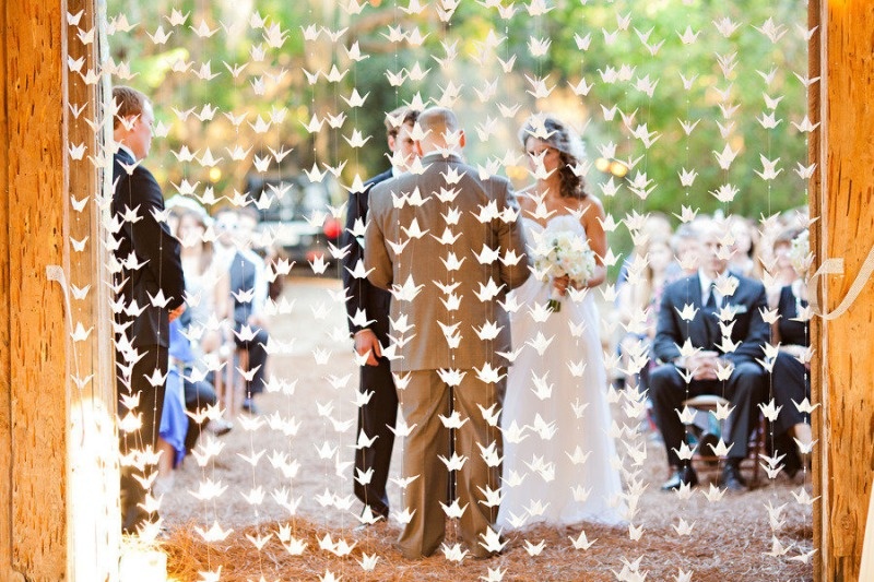 a stained wedding arch with white origami cranes hanging is a gorgeous idea for a modern wedding with a bit of DIY