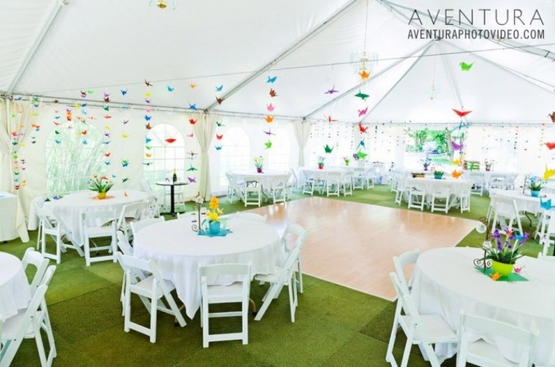 a neutral wedding reception space with colorful origami crane garlands over each table that are a lovely idea that you can DIY