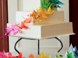 a square white wedding cake decorated with colorful origami cranes with a gradient effect is a fantastic idea