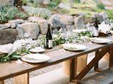 a neutral and nautral tablescape with greenery and uncovered wooden tables and benches for a mountain wedding