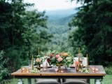 a sweetheart table decorated with greenery and blooms and placed right in the mountains