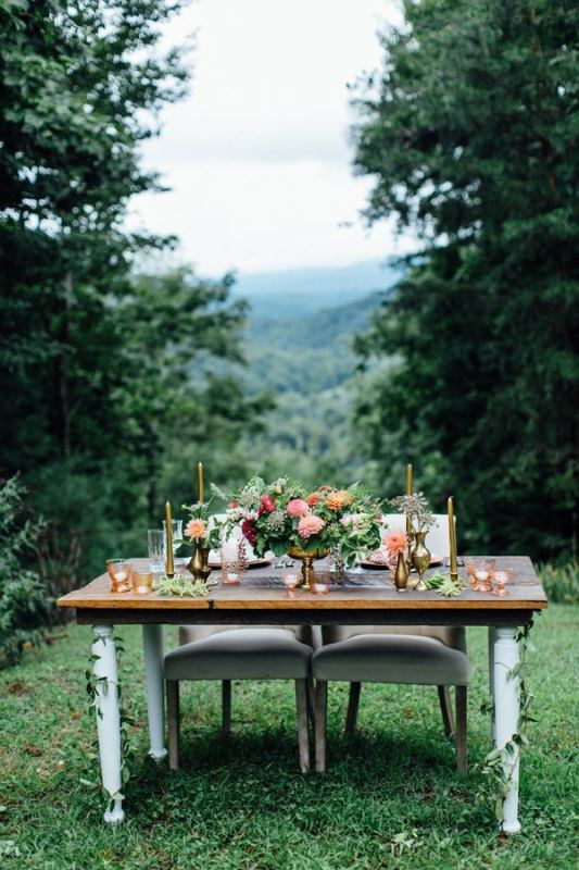 A sweetheart table decorated with greenery and blooms and placed right in the mountains