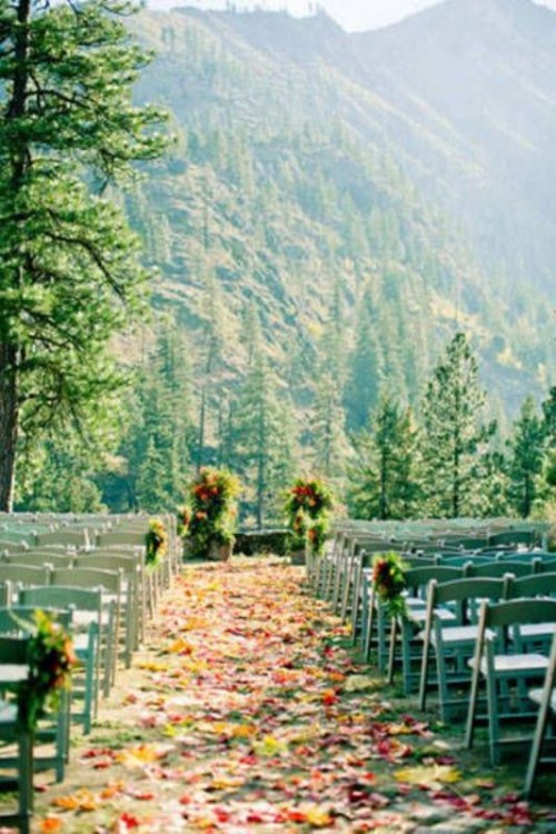 a beautiful wedding ceremony space done with colorful fall leaves and petals, greenery and a fantastic mountain view