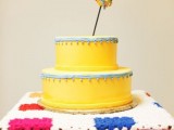 a bold and cool yellow wedding cake with blue ribbons with bells and a bold yarn heart topper is a whimsy dessert idea