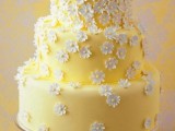 a cute and lovely yellow wedding cake with white sugar blooms covering it is amazing for a spring or summer wedding