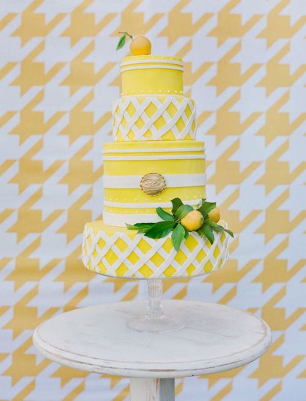 A bright and cool yellow and white wedding cake with striped tiers and tiers that imitate pie covers, lemons and greenery is all fun