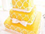 a yellow square wedding cake with white ribbons and a bow and white patterns is a great idea for a vintage wedding