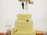 a pale yellow textural wedding cake with white blooms and cake toppers, with the couple’s names is a cool idea