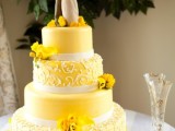 a bold yellow wedding cake with plain and patterned tiers, with yellow blooms and a traditional cake topper is fun