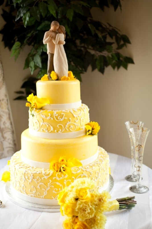 A bold yellow wedding cake with plain and patterned tiers, with yellow blooms and a traditional cake topper is fun