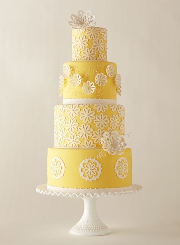 A yellow and white patterned wedding cake with sugar blooms that are dimensional and usual and a sugar bloom on top