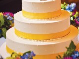 a white patterned wedding cake with yellow ribbons, beads and bold blooms on top is a bright and fun idea
