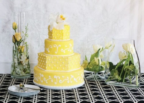a bold yellow wedding cake with white beads and patterns and a white bloom on top is a pretty dessert for spring or summer