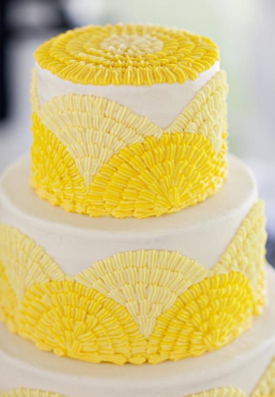 A white wedding cake with pale and bright yellow sugar patterns and some of them on top is a fun and bold idea