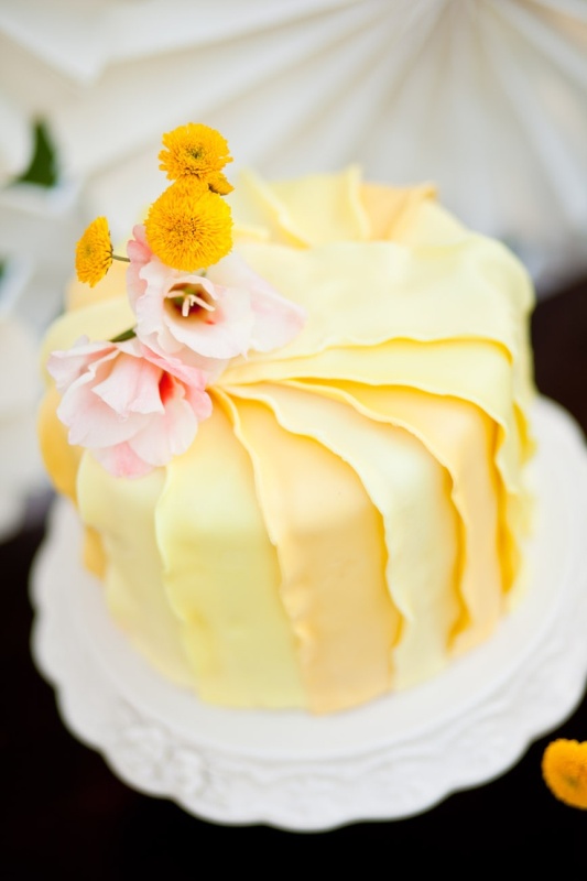 A yellow ruffled tiered wedding cake with pink and yellow blooms is a lovely and refined idea for a vintage wedding