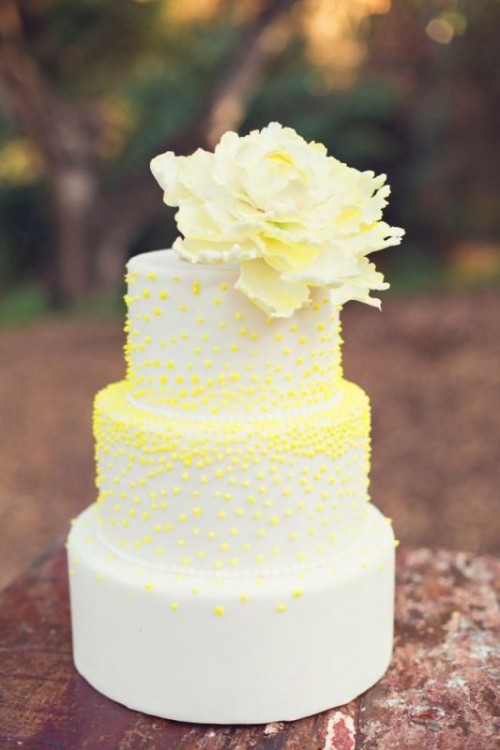 a fun white wedding cake with yellow polka dots and a sugar bloom on top is a playful and whimsical idea