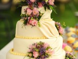 an ivory wedding cake with yellow beads and tiers of sugar, with bright fresh blooms and greenery