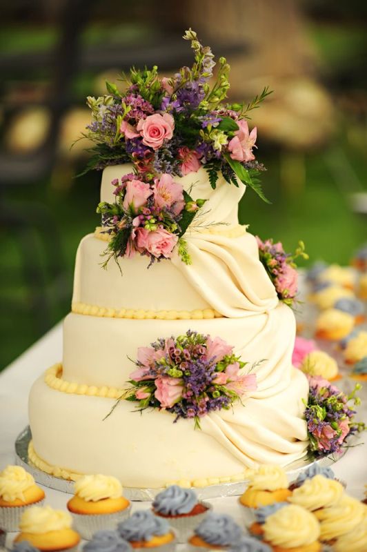 An ivory wedding cake with yellow beads and tiers of sugar, with bright fresh blooms and greenery