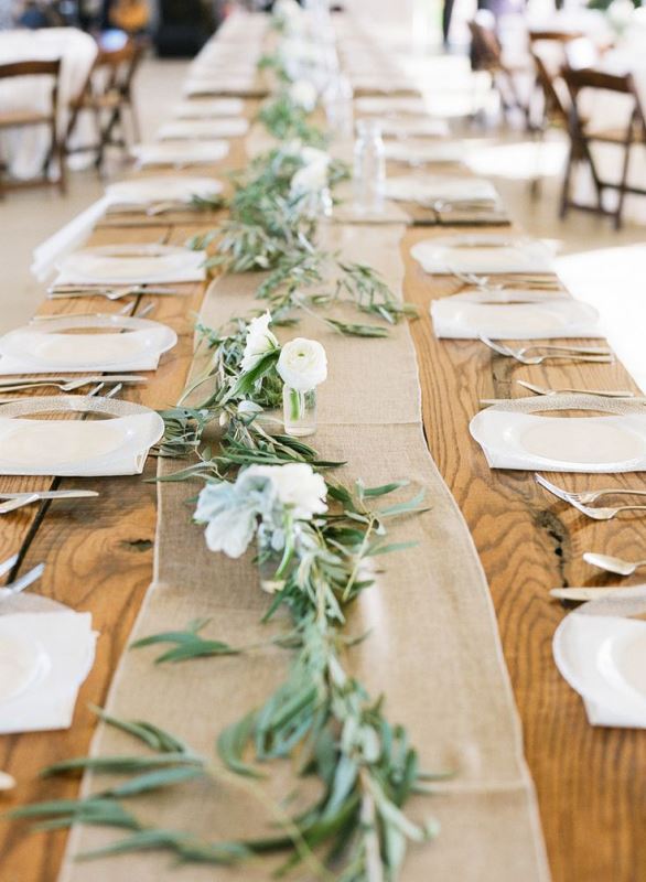 A simple wedding table runner of olive foliage and white blooms plus a burlap runner to pair it with are a cool rustic combo