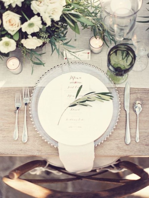 a place setting with an olive branch and a matching green glass for a rustic modern tablescape