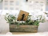 a reclaimed wooden box with olive greenery and a table number is a nice and simple wedding centerpiece idea