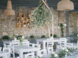 a olive greenery chandelier and matching table runners with candles and white blooms is a cool rustic setup for a wedding venue