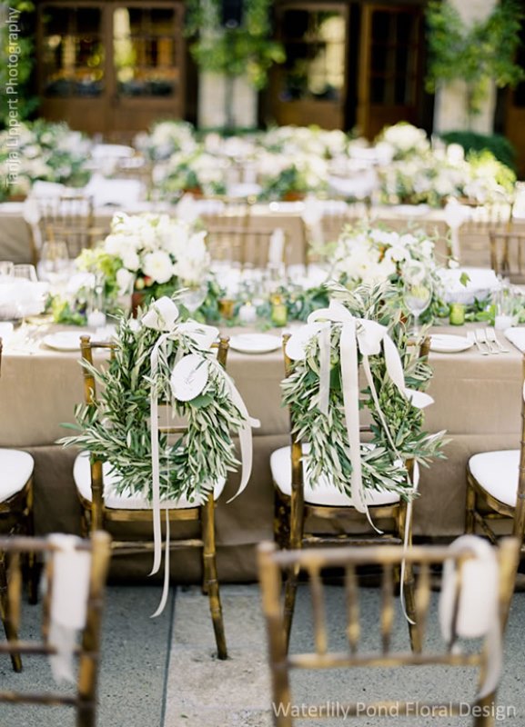 Lush olive foliage wreaths with white bows are a nice substitute to usual signage and markers for the couple's chairs