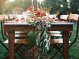 a fall wedding table runner with olive greenery, dried greenery and foliage and pomegranates and other fruits